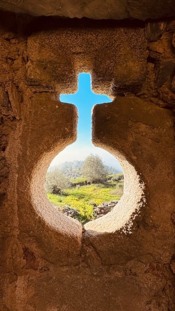 a window in a stone wall with a view of a cross